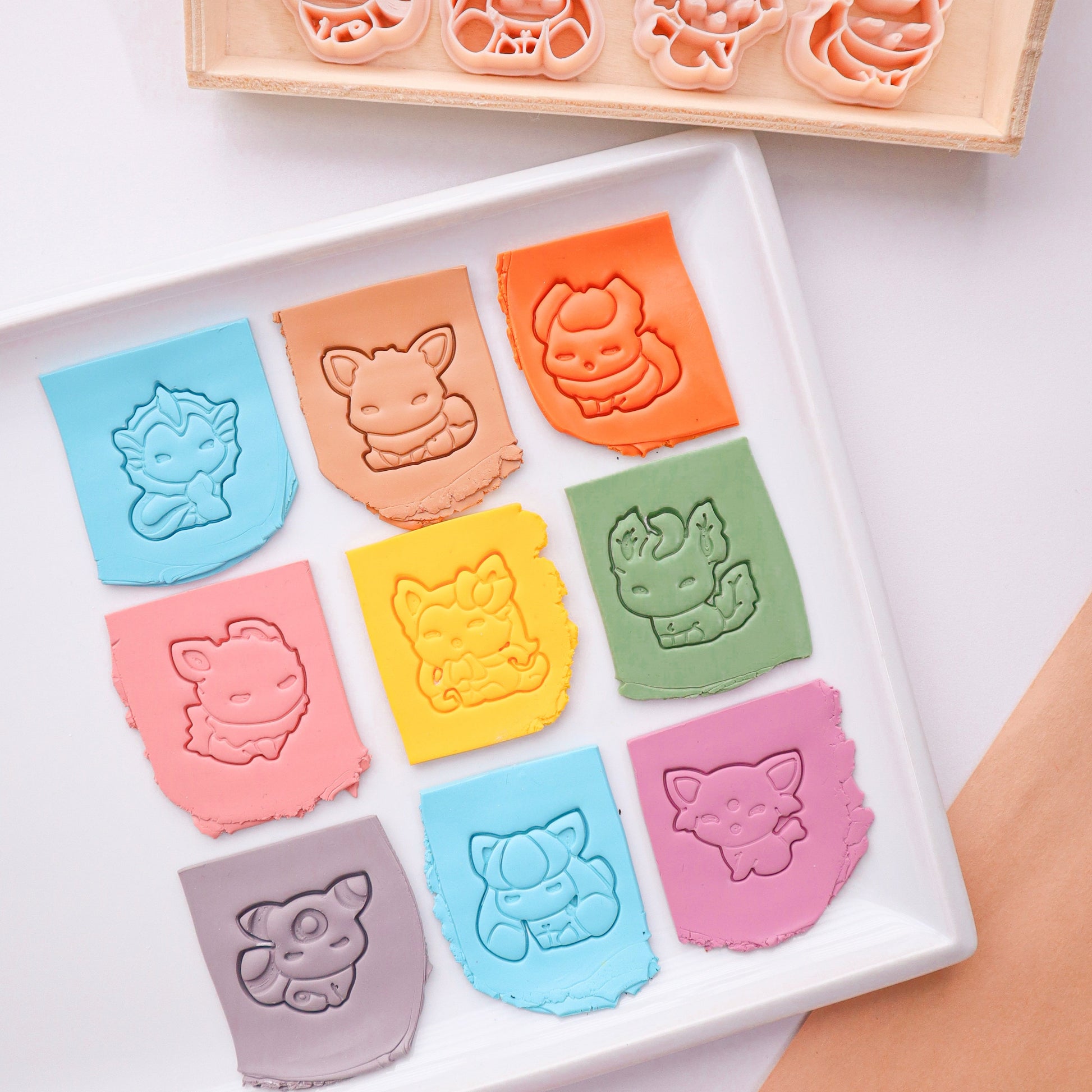 Set of colorful pokemon-shaped clay cutters on a white tray with a wooden holder.