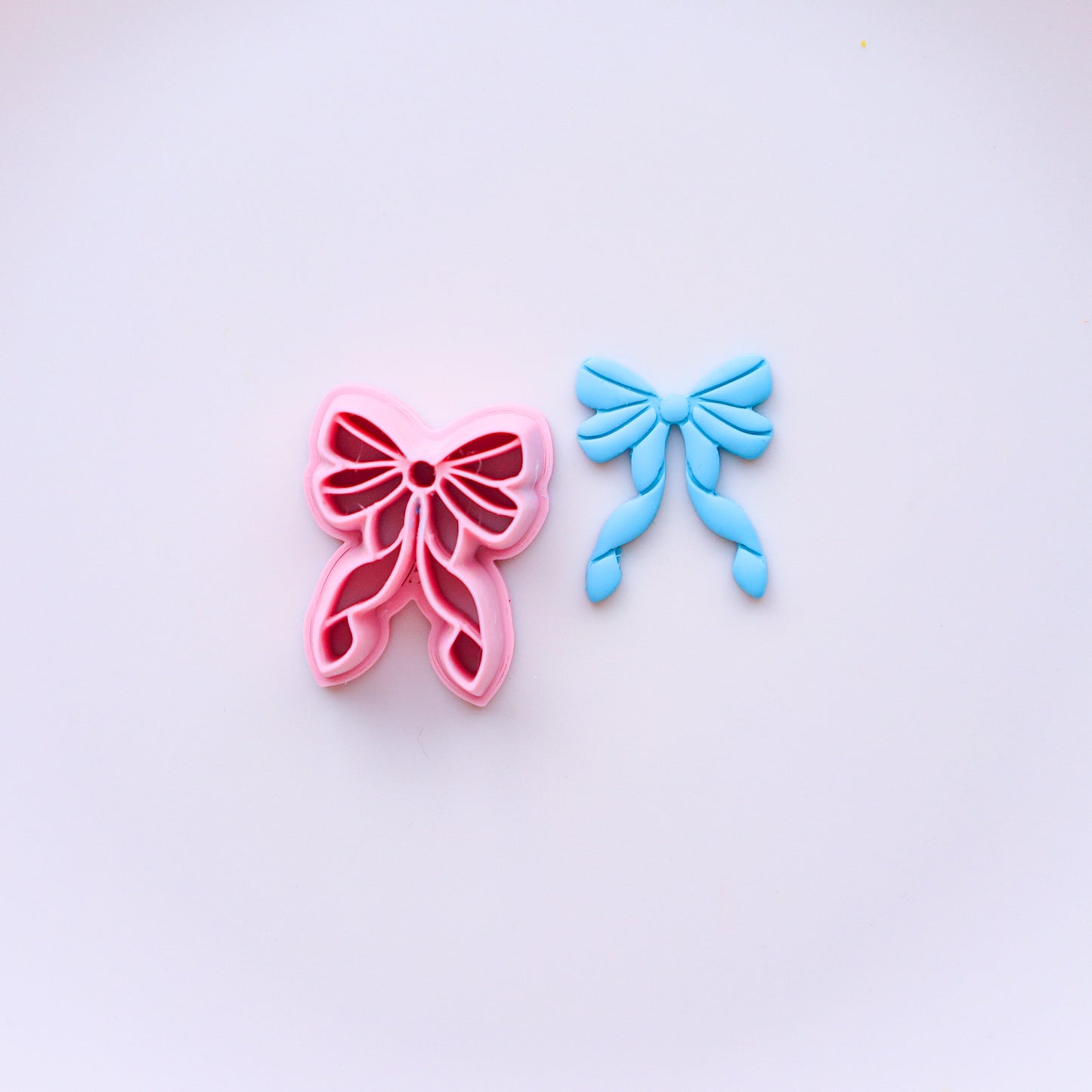 Pink and blue bow-shaped clay cutters on a light purple background