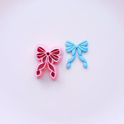 Pink and blue bow-shaped clay cutters on a light purple background